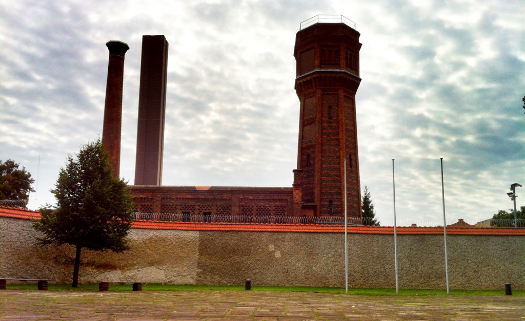 Sicht vom Innenhof der Gedenkstätte Plötzensee über eine Mauer mit Stacheldraht. Dahinter ragen große rote Türme aus Backsteinziegeln empor.